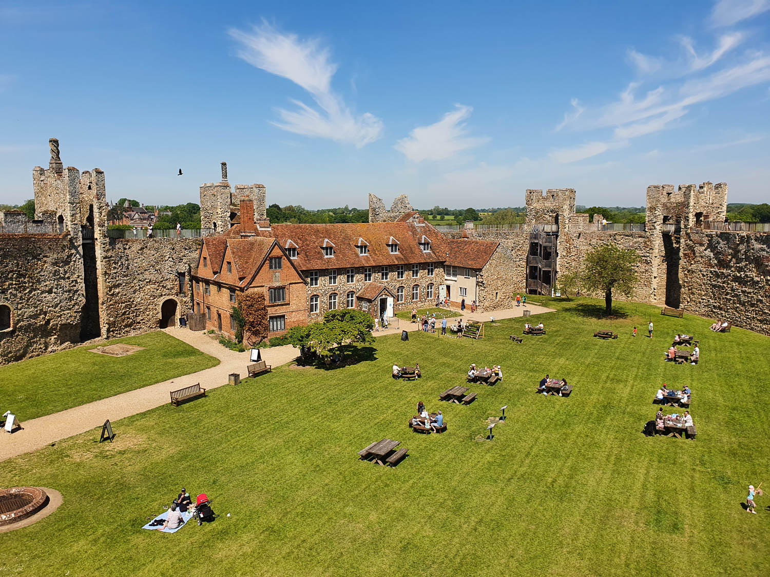 View across the grass of inner court with picnic tables to the stone towers and old workhouse on a day out at Framlingham Castle with kids