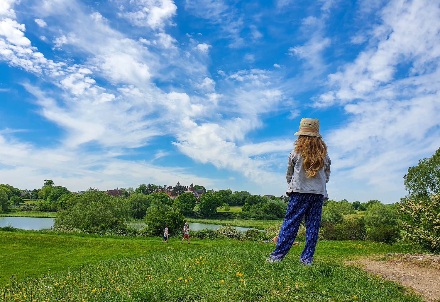 View of my daughter standing among the grass and wildflowers looking out to the mere behind Framlingham Castle, Suffolk on a summer day