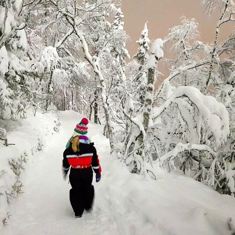 My daughter walks along a snowy path among the trees in Levi, Finnish Lapland - ideas of what to do in Levi with kids on a Lapland Santa break