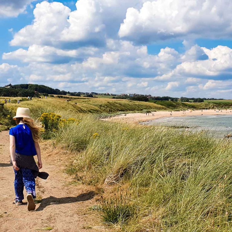My daughter walks along the cliff path towards Embleton Beach and the sea during our holiday in Northumberland with kids