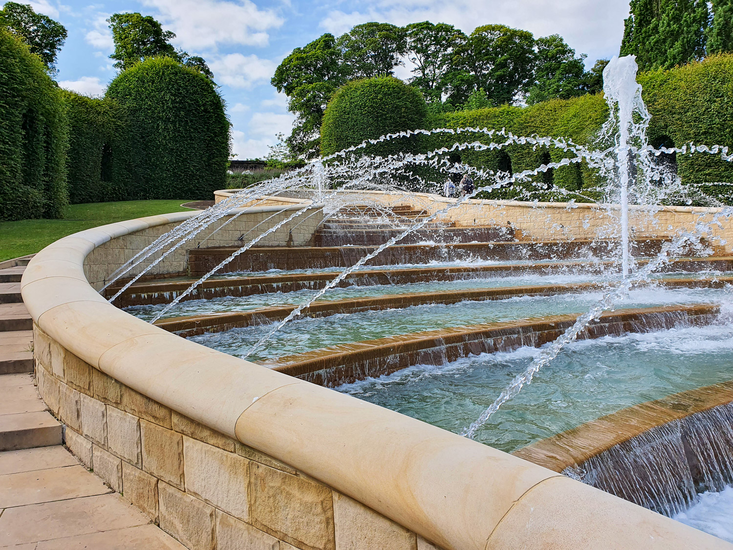 Close up of jets of water spraying across waterfall steps of the Grand Cascade with hedges in the background - a day out at Alnwick Garden with kids