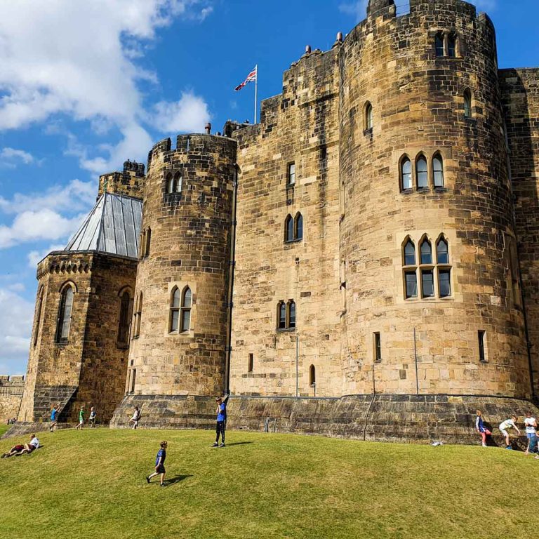 View up to the towers and turrets of Alnwick Castle with kids playing on the grassy slopes - my review of Alnwick Castle, Northumberland