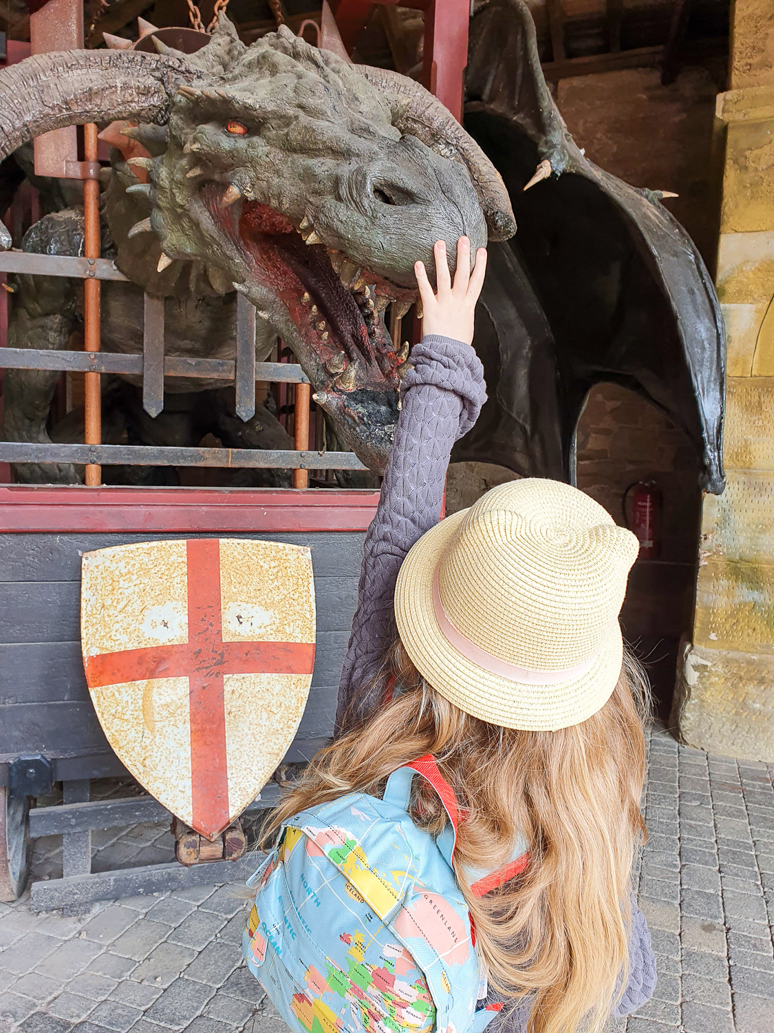 M daughter stretches up her hand towards the nose of a dragon statue in the Artisans Courtyard - my review of a visit to Alnwick Castle with kids