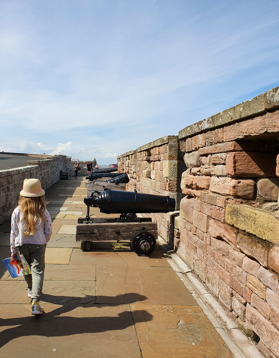 My daughter walks along the walls at Bamburgh Castle, Northumberland past cannon