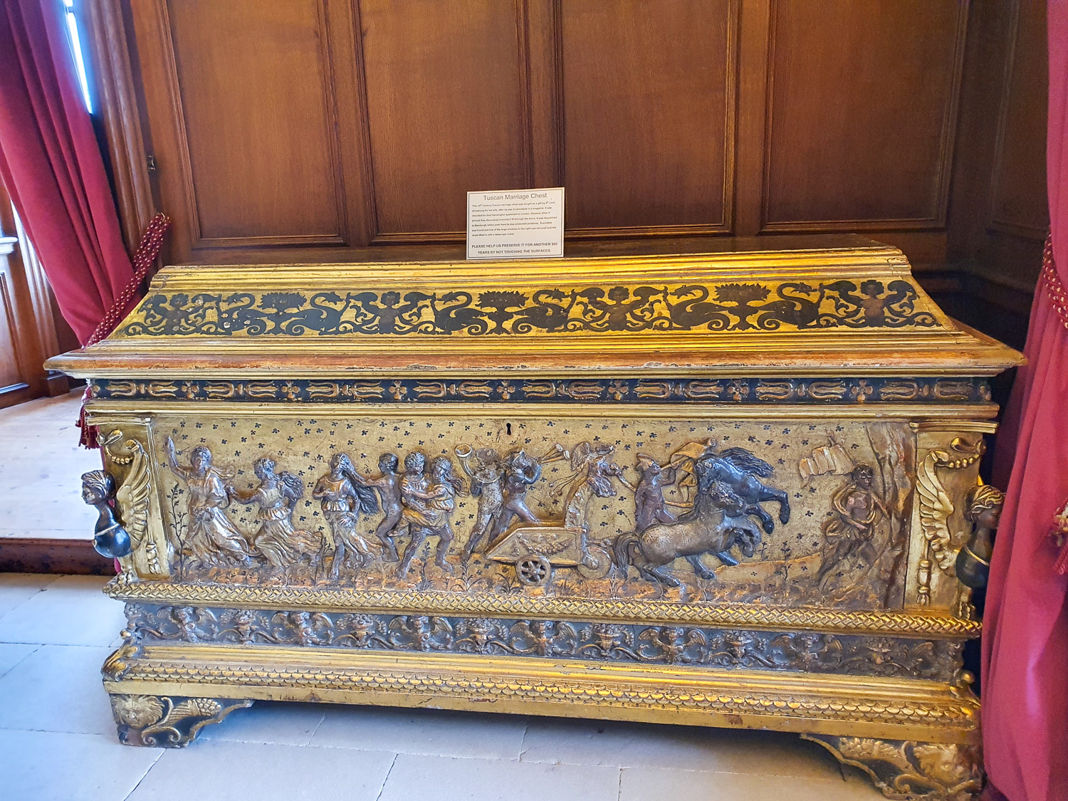 Ornate Tuscan marriage chest on display at Bamburgh Castle, Northumberland, with gold decoration and carved figures of people and horses
