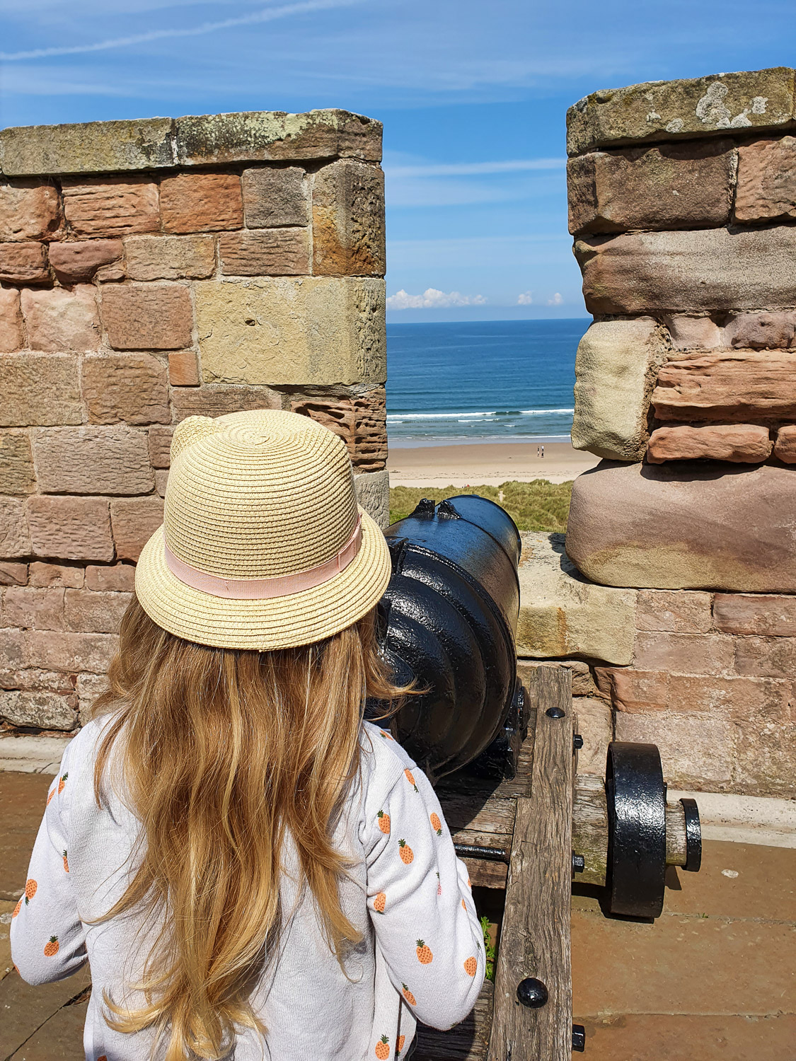 My daughter stands by a cannon pointing out to the beach and sea during a visit to Bamburgh Castle with kids