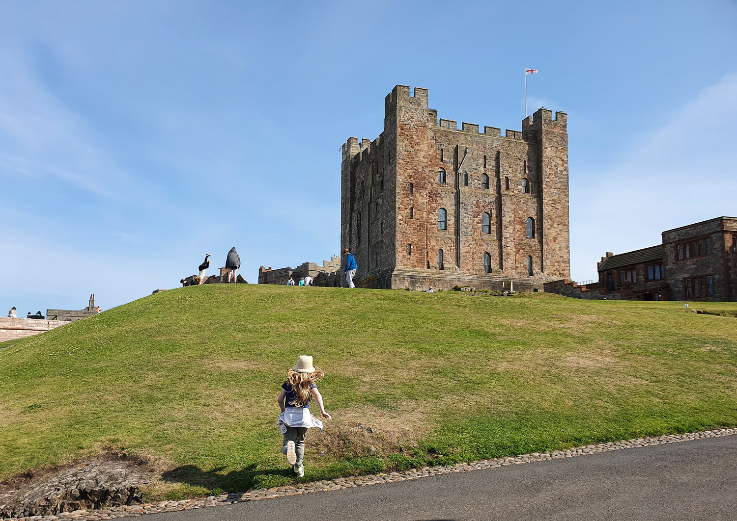 My daughter races up the grassy mound towards the old square tower of the Keep during a day out at Bamburgh Castle with kids