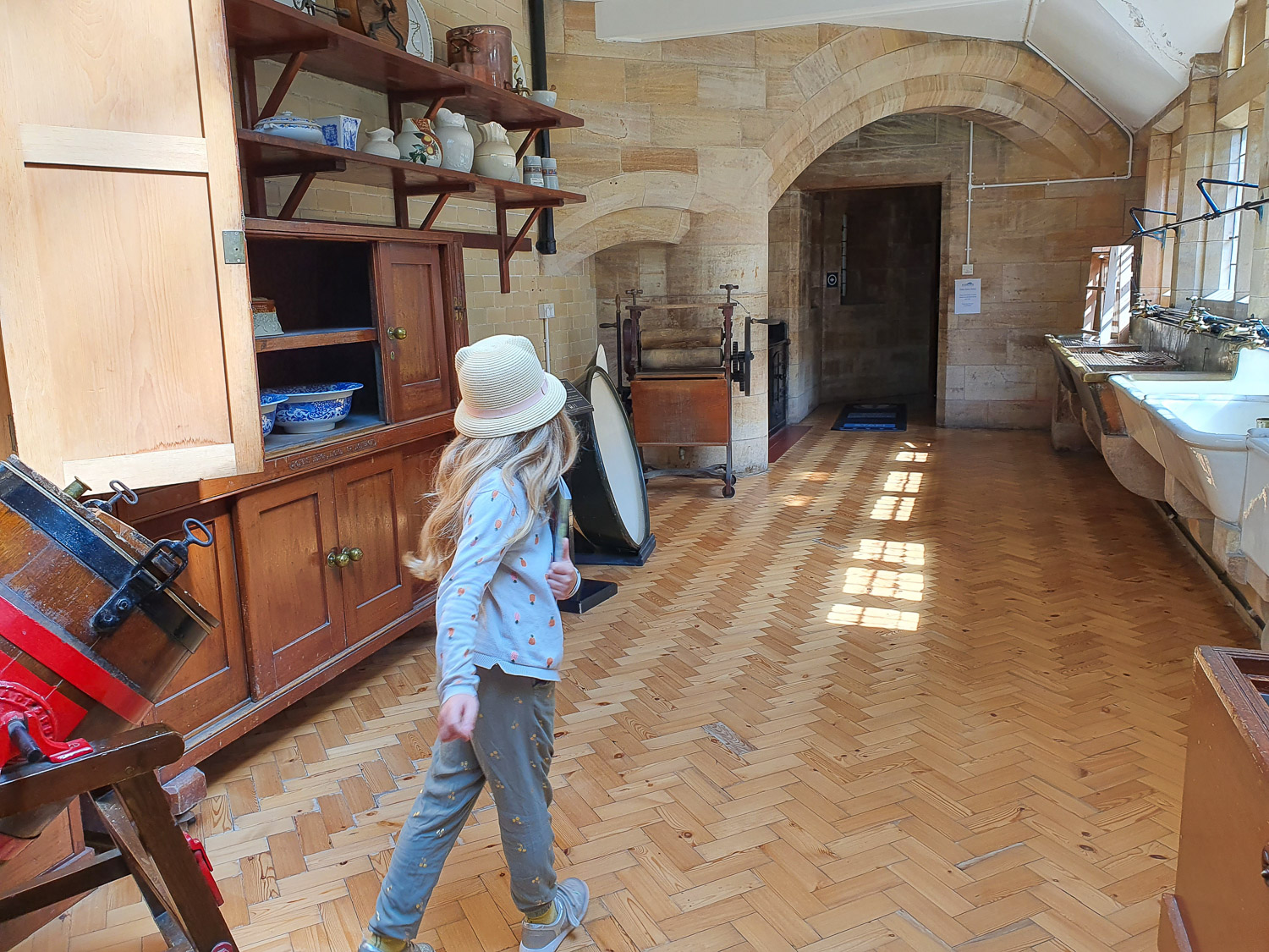 My daughter walks through the old kitchens with churn and old jugs on display - a day out at Bamburgh Castle with kids