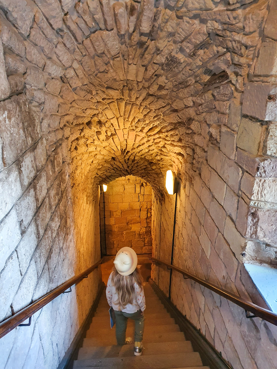 My daughter walks down the stairs towards the underground vaults at Bamburgh Castle, Northumberland, with an arched stone ceiling above