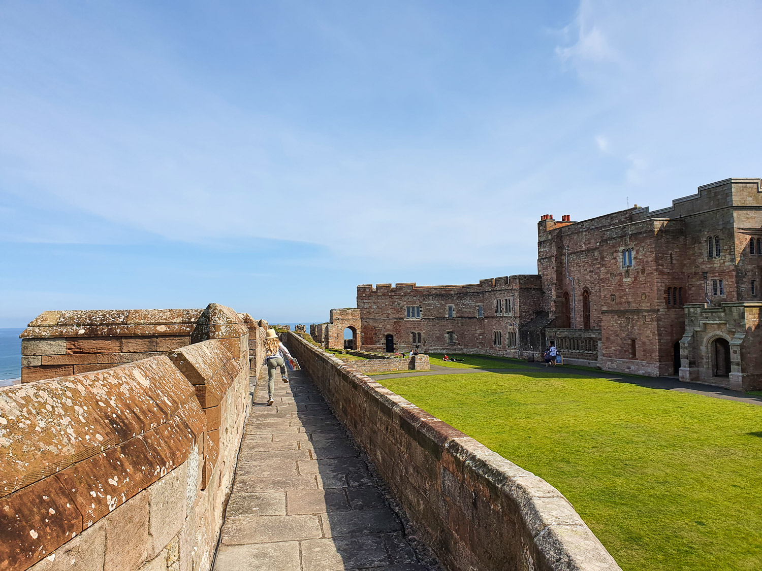 View of my daughter galloping along the wall walk with part of the old castle buildings seen to the side - my review of a day at Bamburgh Castle with kids