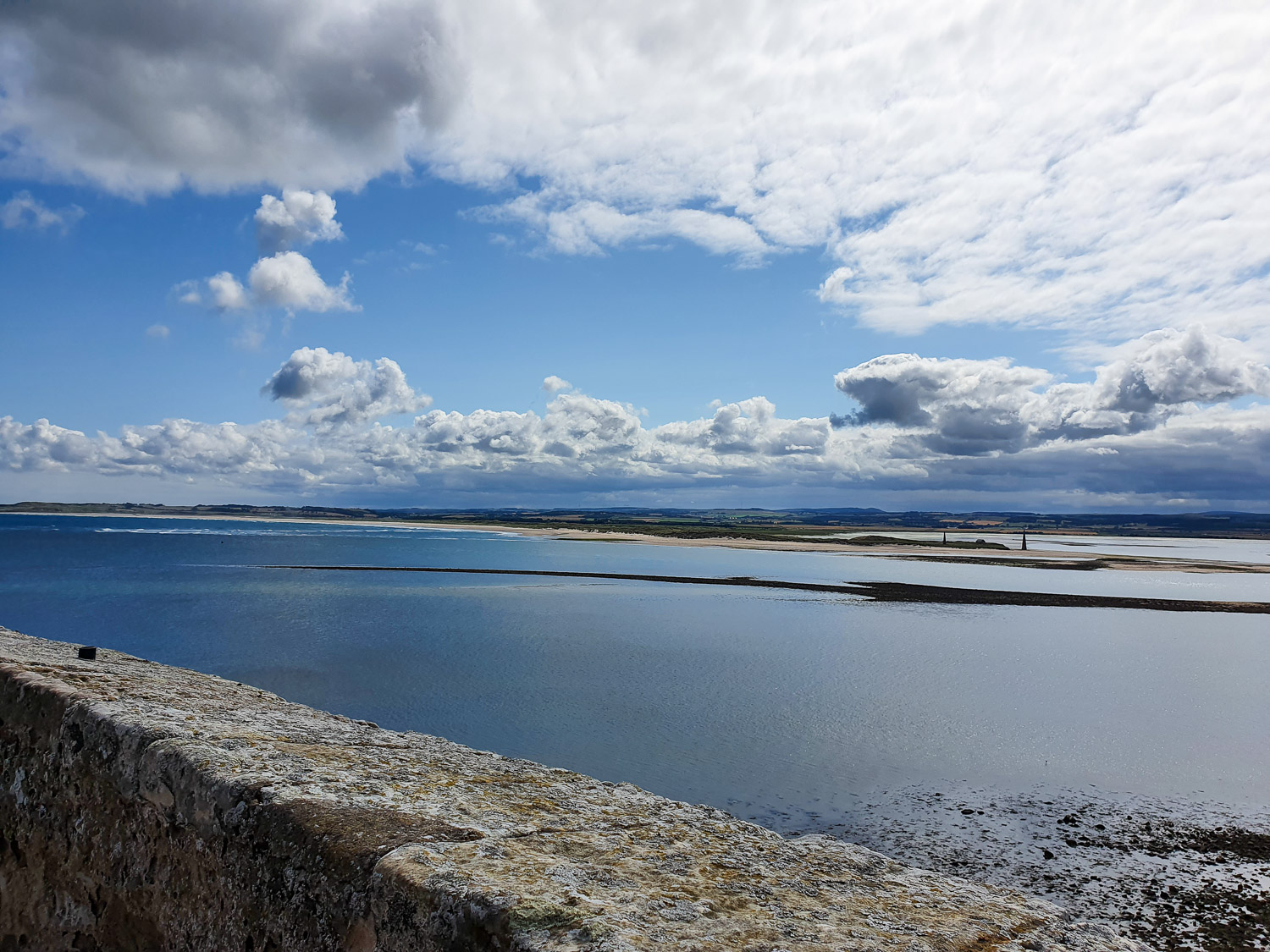 View over a wall to the calm sea and land beyond from the Upper Battery of Lindisfarne Castle - you'll find some of the best views on Lindisfarne from here
