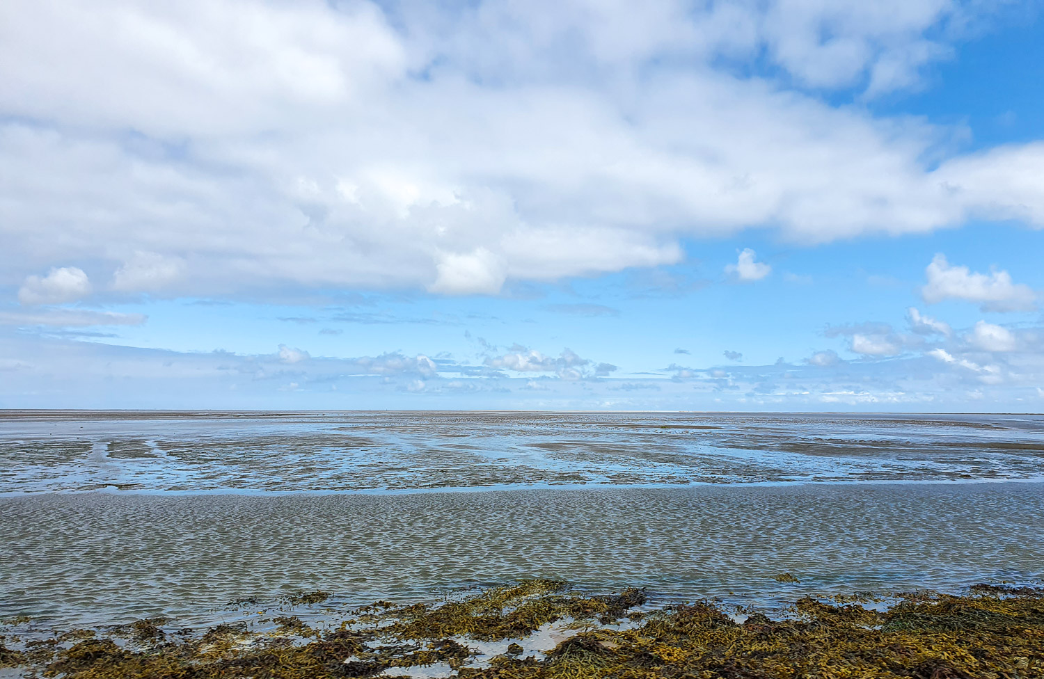 View across the mud flats with the waves of receding water from the causeway to Lindisfarne Island during a family day out in Northumberland