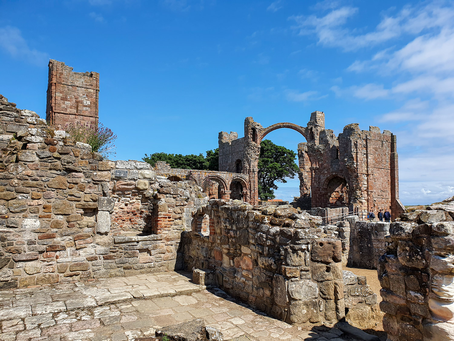 View across the low stone walls of one of the old rooms at Lindisfarne Priory to the arch of the church - one of the best places to visit on Lindisfarne with kids