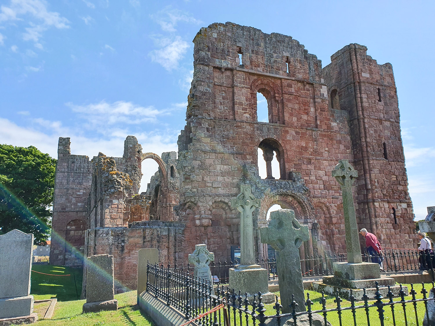 View across gravestones in St Mary's church to the reddish exterior wall of the ruined Lindisfarne Priory during a visit to Holy Island, Northumberland with kids