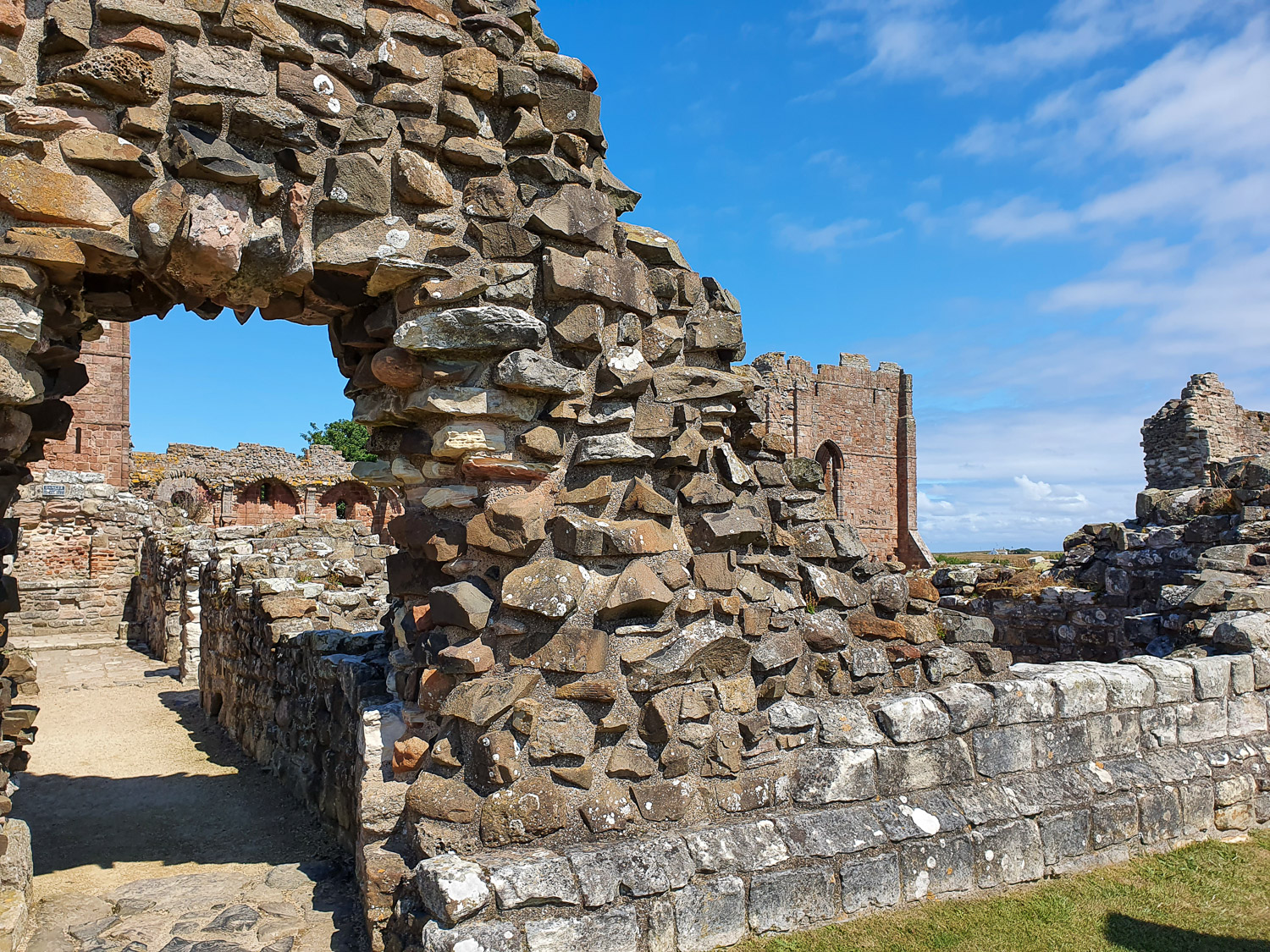 View through a rock arch to ruined rooms and a tower of Lindisfarne Priory during a day out on Lindisfarne, Northumberland with kids