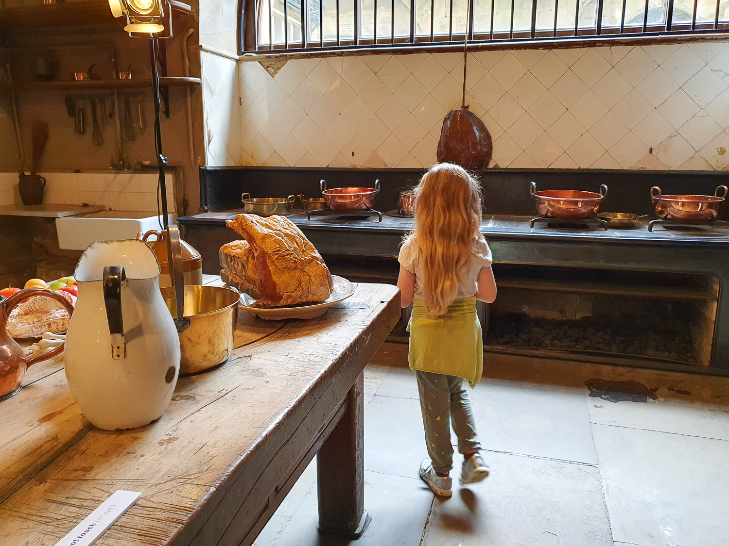 My daughter walks through the kitchens below stairs at Harewood House, including replica meat and copper pans in the background - a day out at the historic house in Yorkshire