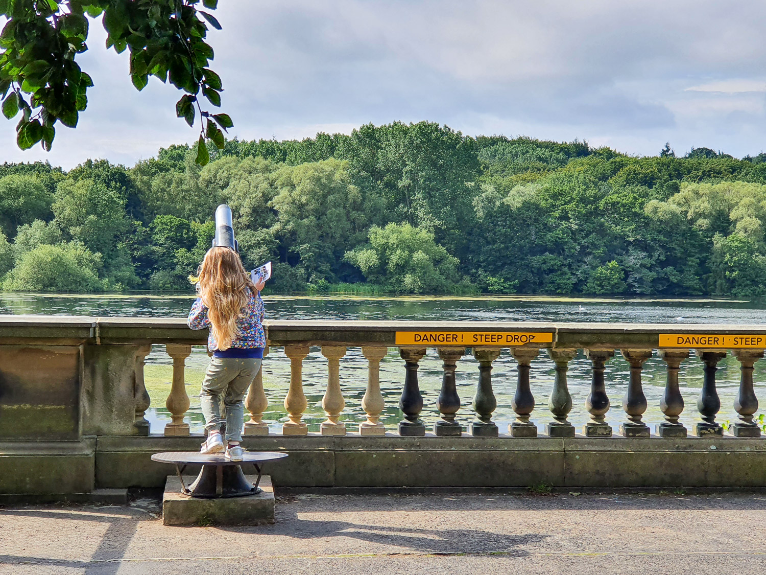 My daughter looks through a telescope across the lake during a day out at Harewood House with kids
