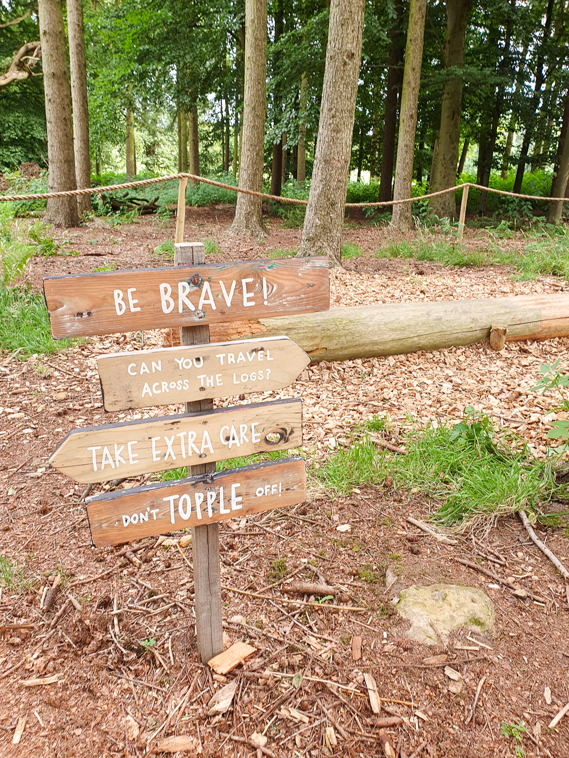 Signpost saying 'Be Brave, can you travel across the logs, take extra care, don't topple off' in the natural playground at Harewood House in Yorkshire