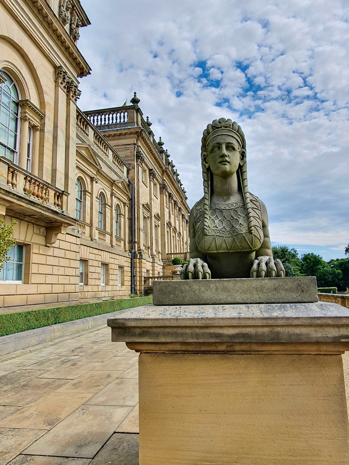 Sphinx statue on a plinth around the back of Harewood House, seen against a cloudy blue sky - a day out at Harewood House with kids
