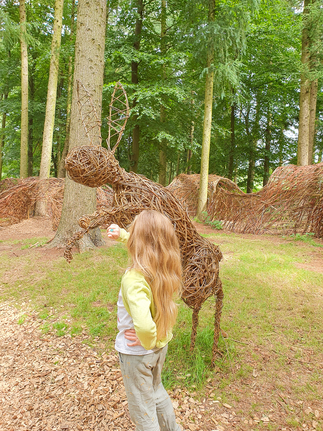 My daughter stretches out her hand towards one of the leaping willow hare sculptures in the natural playground at Harewood House in Yorkshire during a family holiday in Leeds