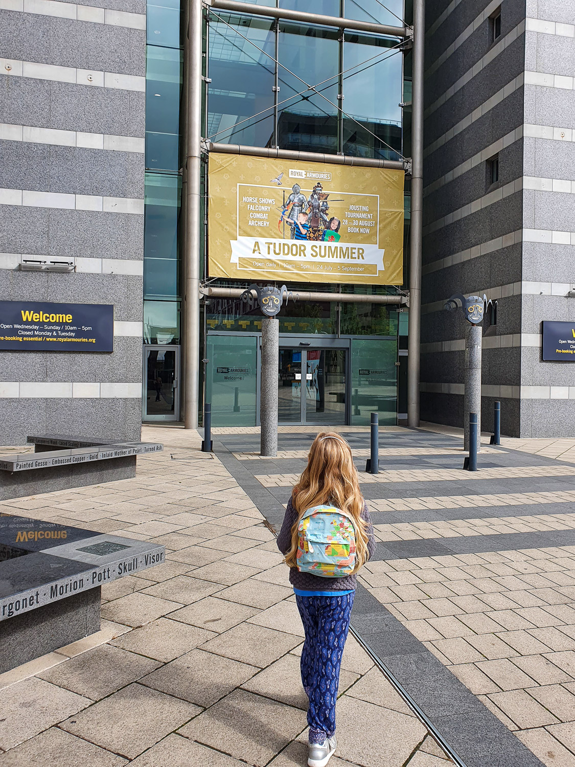 My daughter walks towards the entrance of the Royal Armouries in Leeds, with a sign showing the extra family activities of A Tudor Summer
