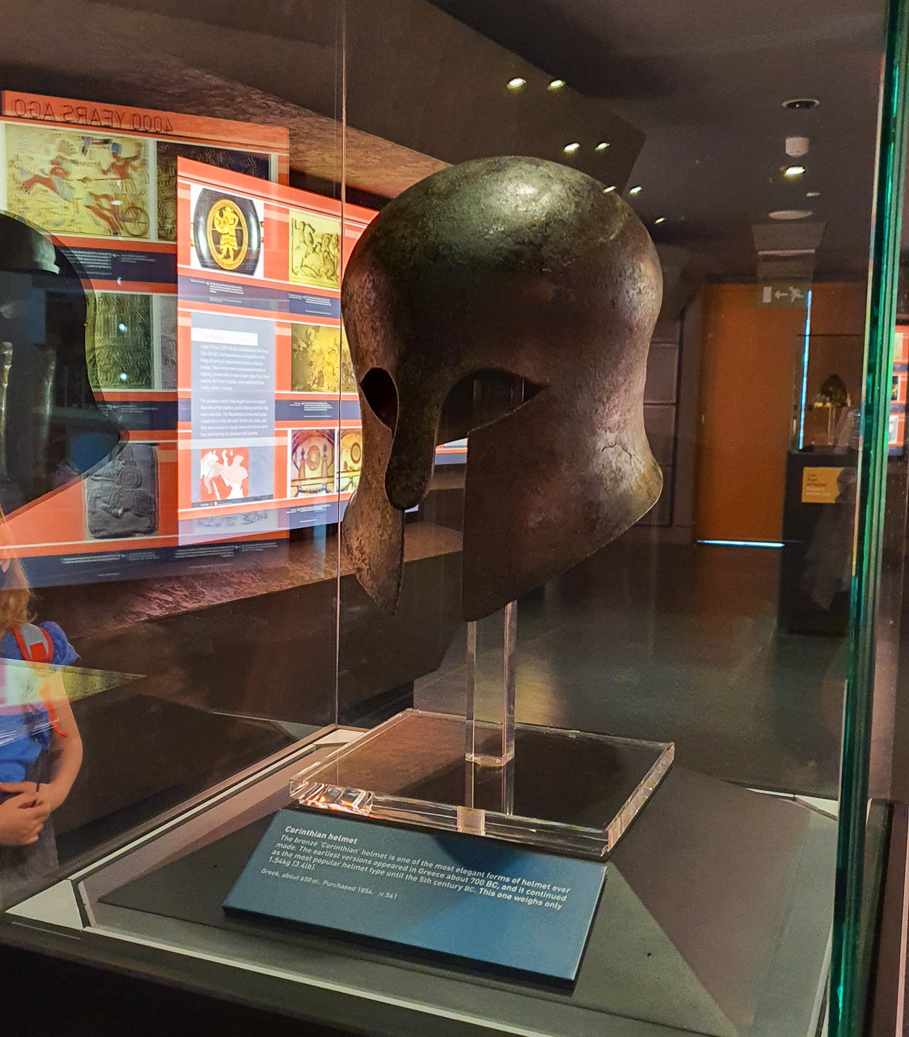 Glass display case with a bronze Corinthian helmet on display in the exhibition on the history of war during a visit to the Royal Armouries with kids