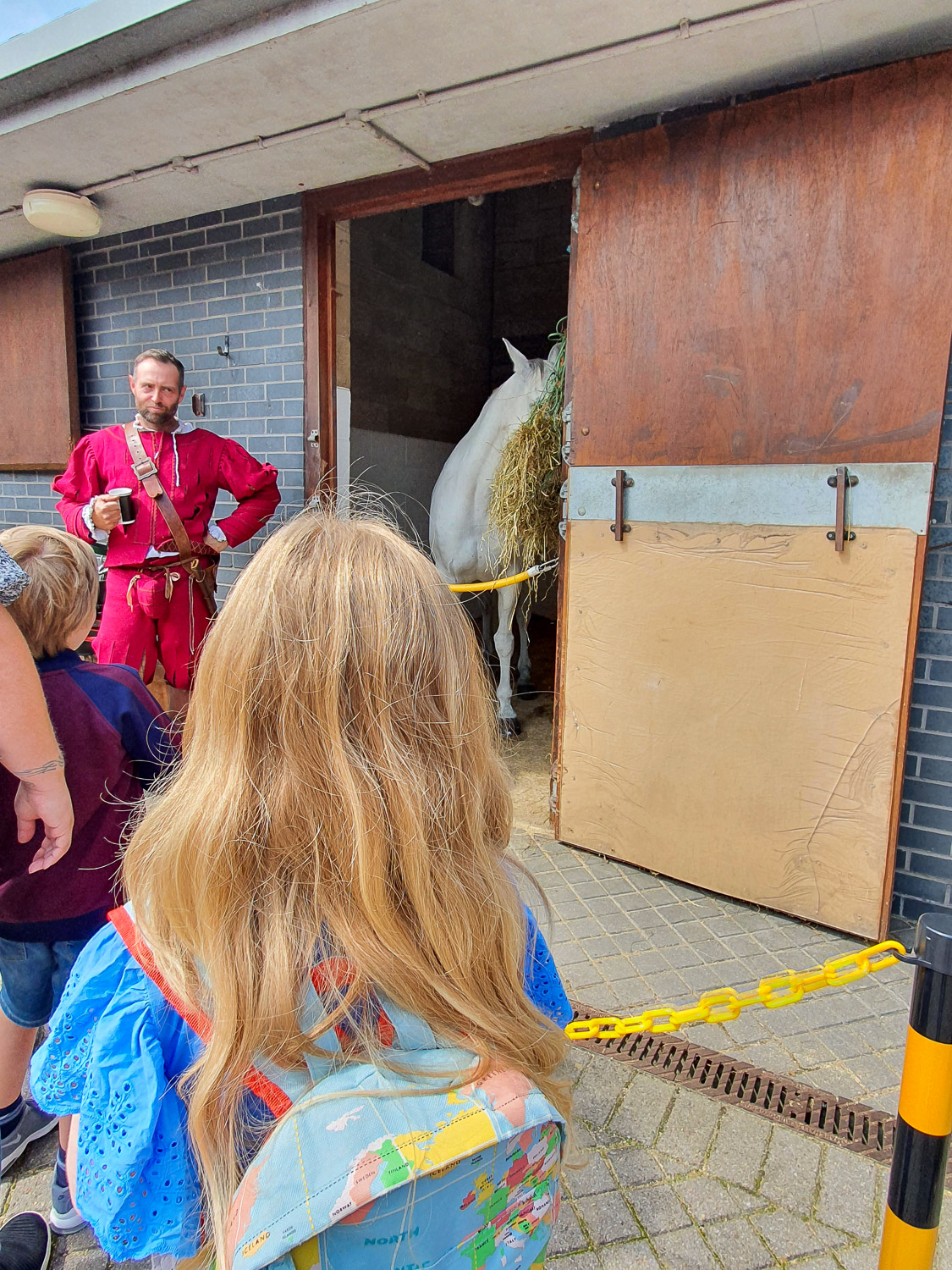 My daughter looks at one of the riders who performed in the tiltyard, his horse just seen in the background with some hay, during a visit to the stables at the Royal Armouries in Leeds