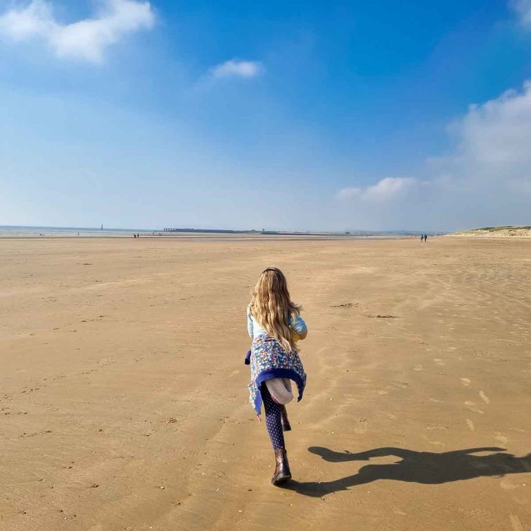 My daughter runs along the smooth empty sand of the beach during a weekend at Camber Sands with kids