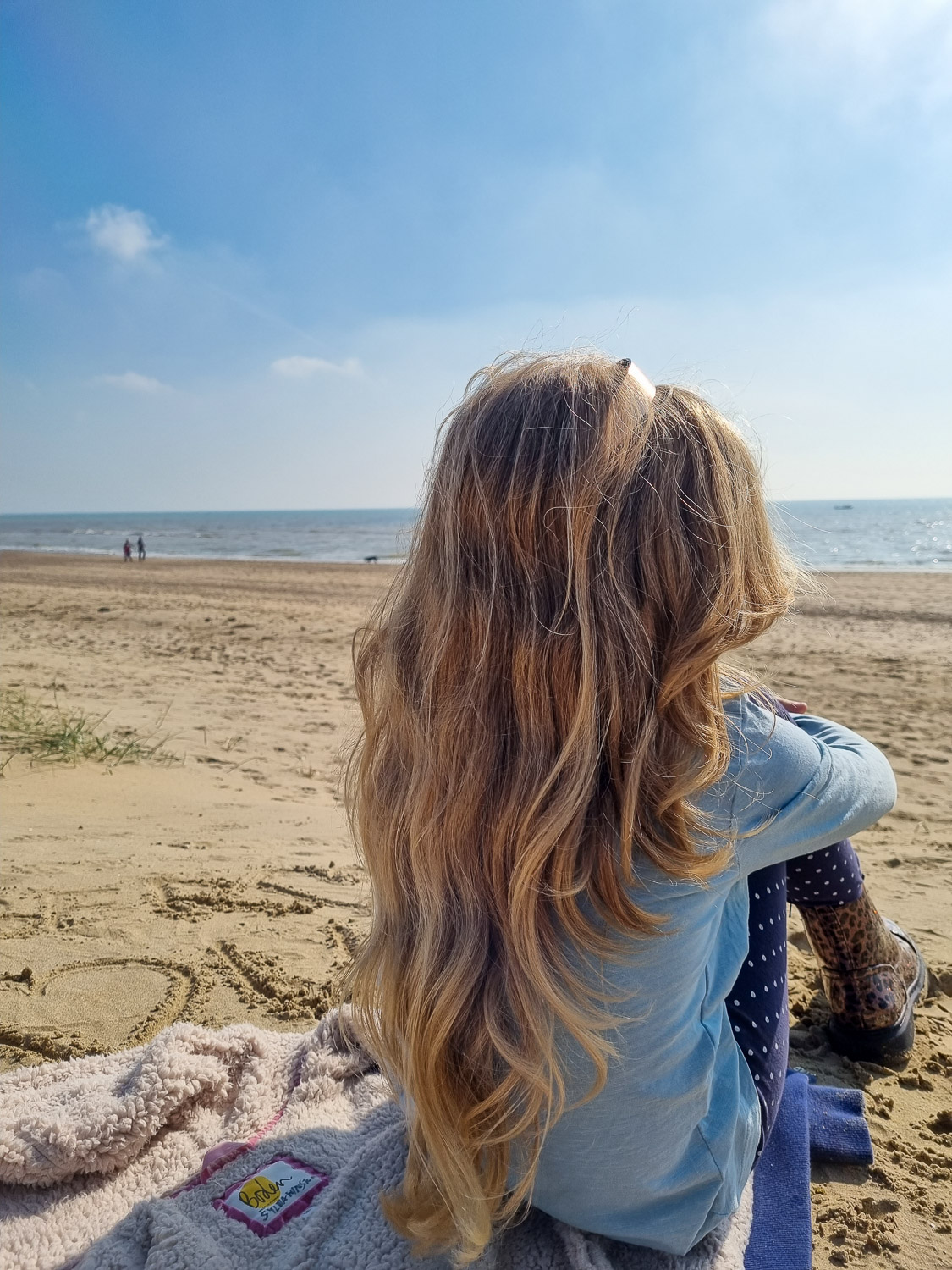 My daughter hugs her knees and looks out to the sea on the beach during a weekend at Camber Sands with kids