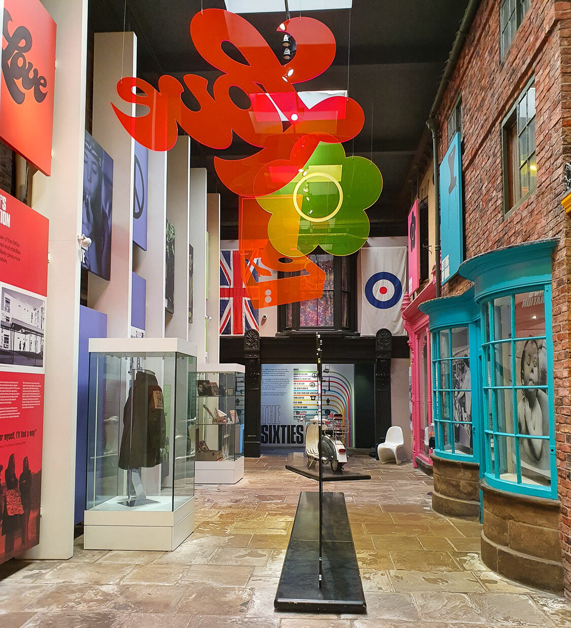 View of the 60s exhibits with a street of brightly coloured shop windows and 60s symbols of flowers and love - my review of York Castle Museum with kids