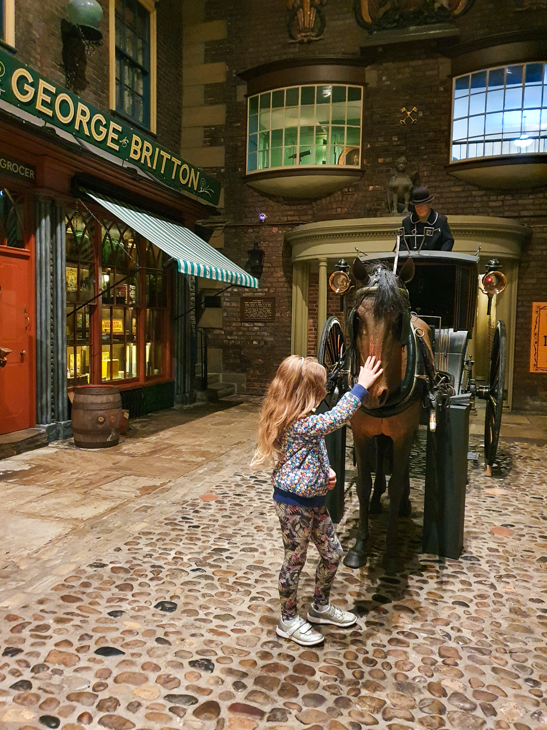 My daughter stretches out to pet the nose of the model horse in the recreated period street at York Castle Museum - my review