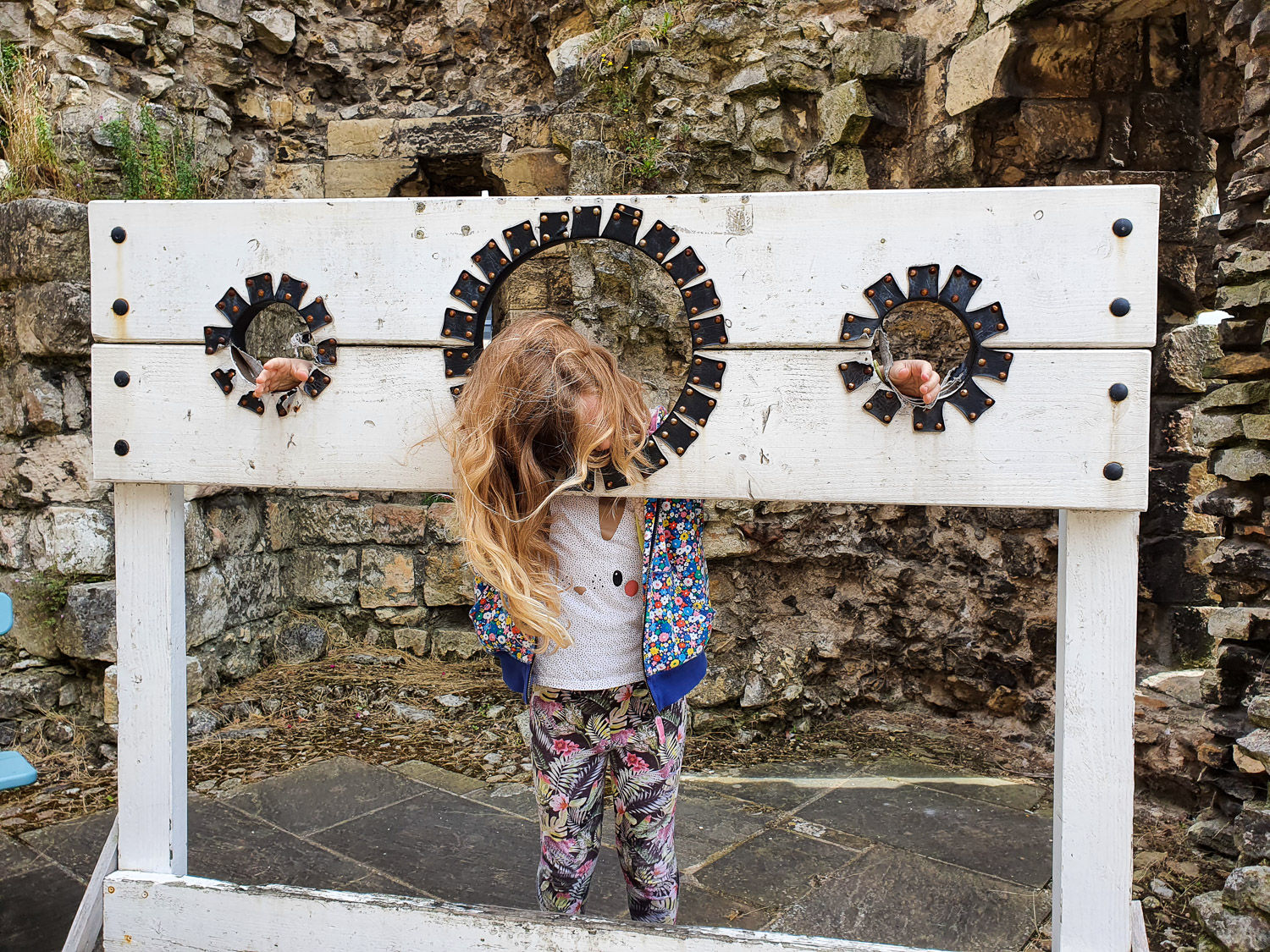 My daughter with her head and hands in the stocks in the exercise yard of York Castle prison during a visit to York Castle Museum with kids