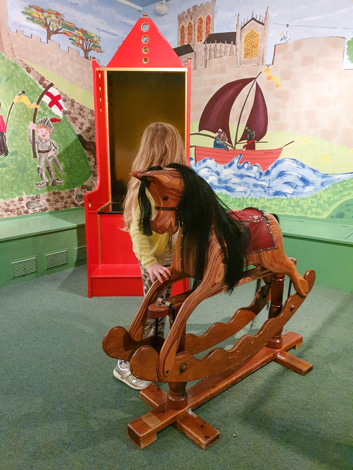 My daughter stands next to an old-fashioned rocking horse in the display of toys at the York Castle Museum, York