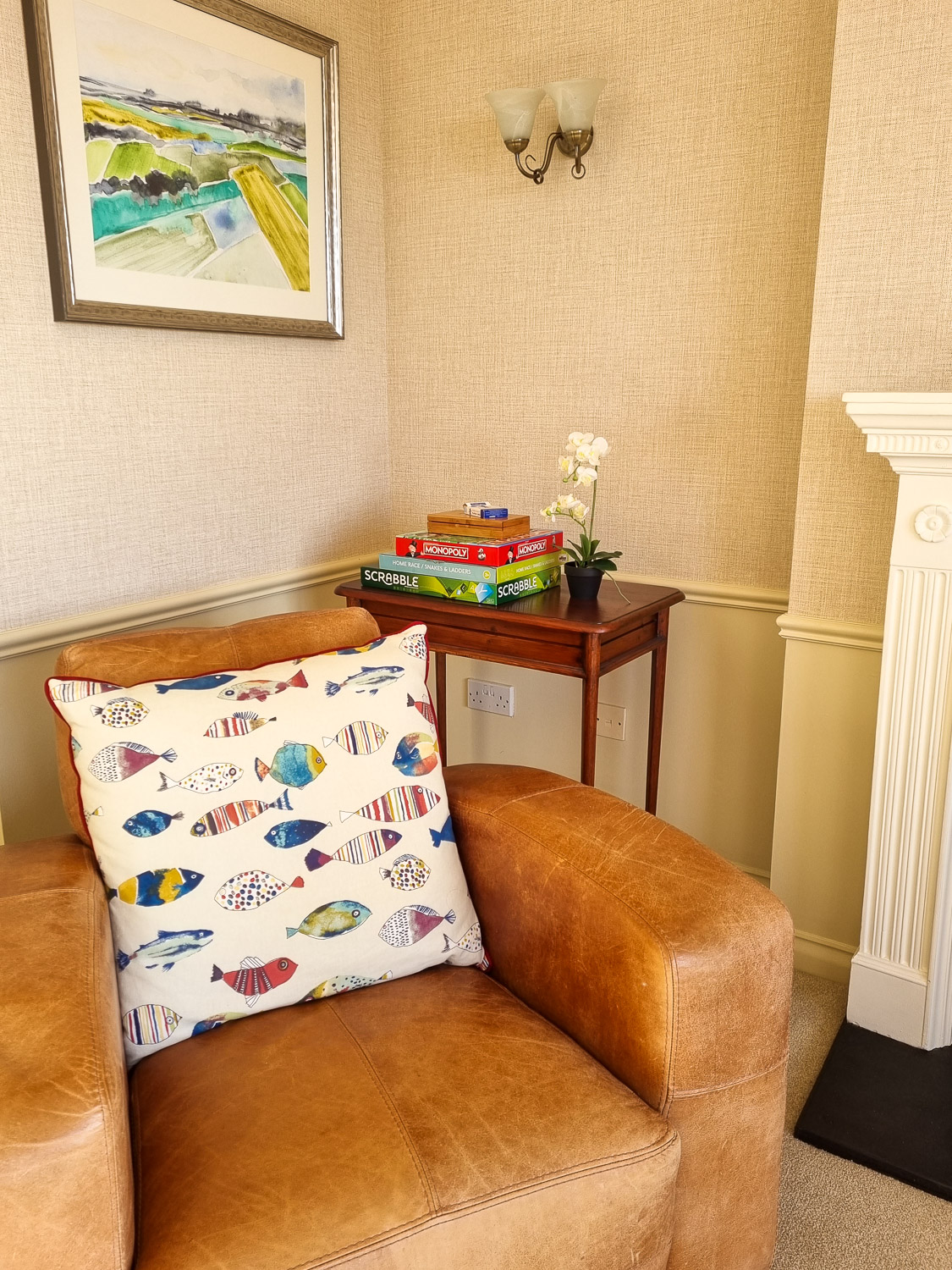 View of one of the light brown leather armchairs with fish cushion and board games on a table in the penthouse at the Beachcroft hotel Felpham - my review of a stay at the Sussex hotel with kids
