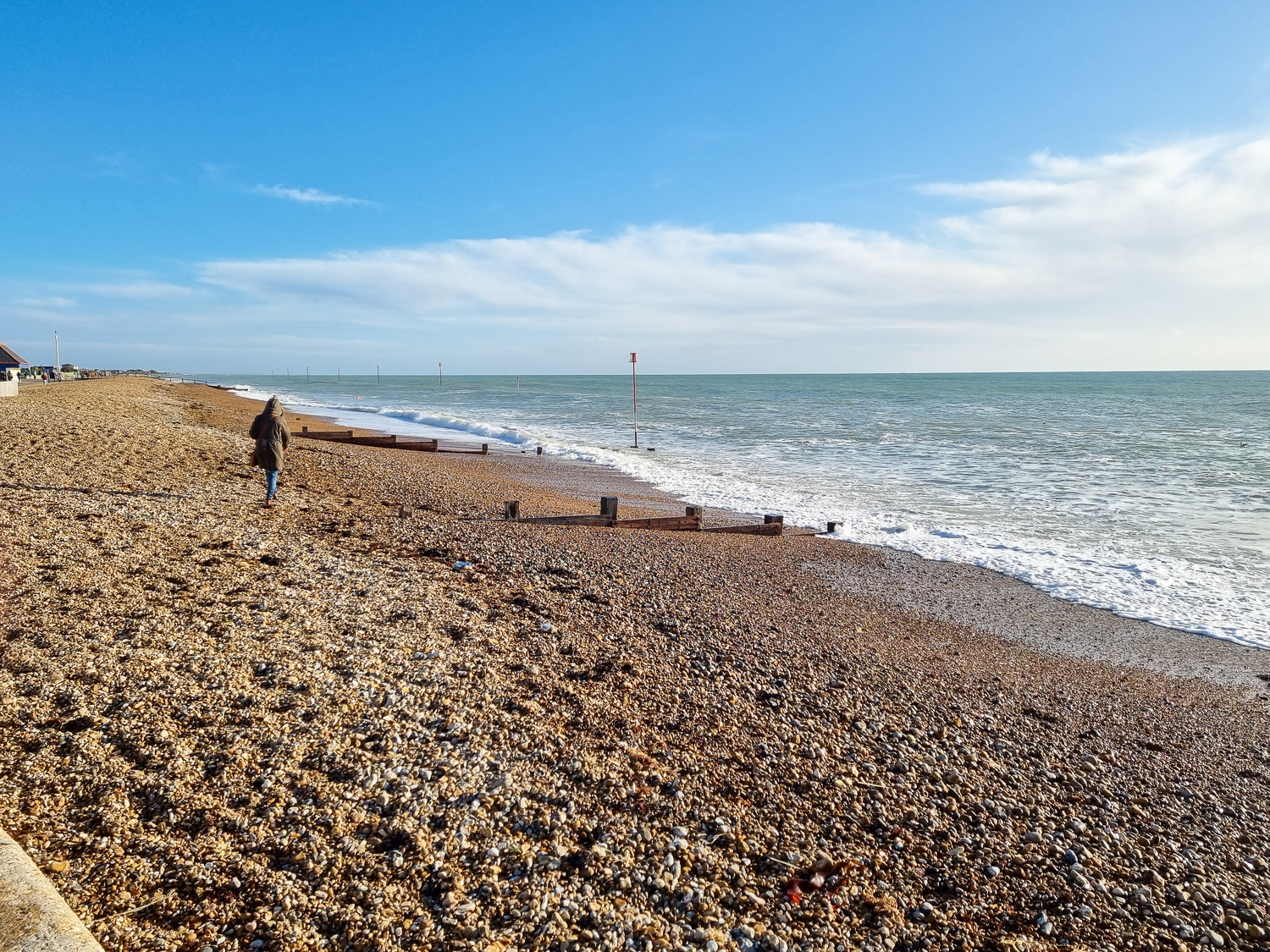 View of a woman walking along the pebble beach at Bognor Regis in west Sussex on a sunny winter's day