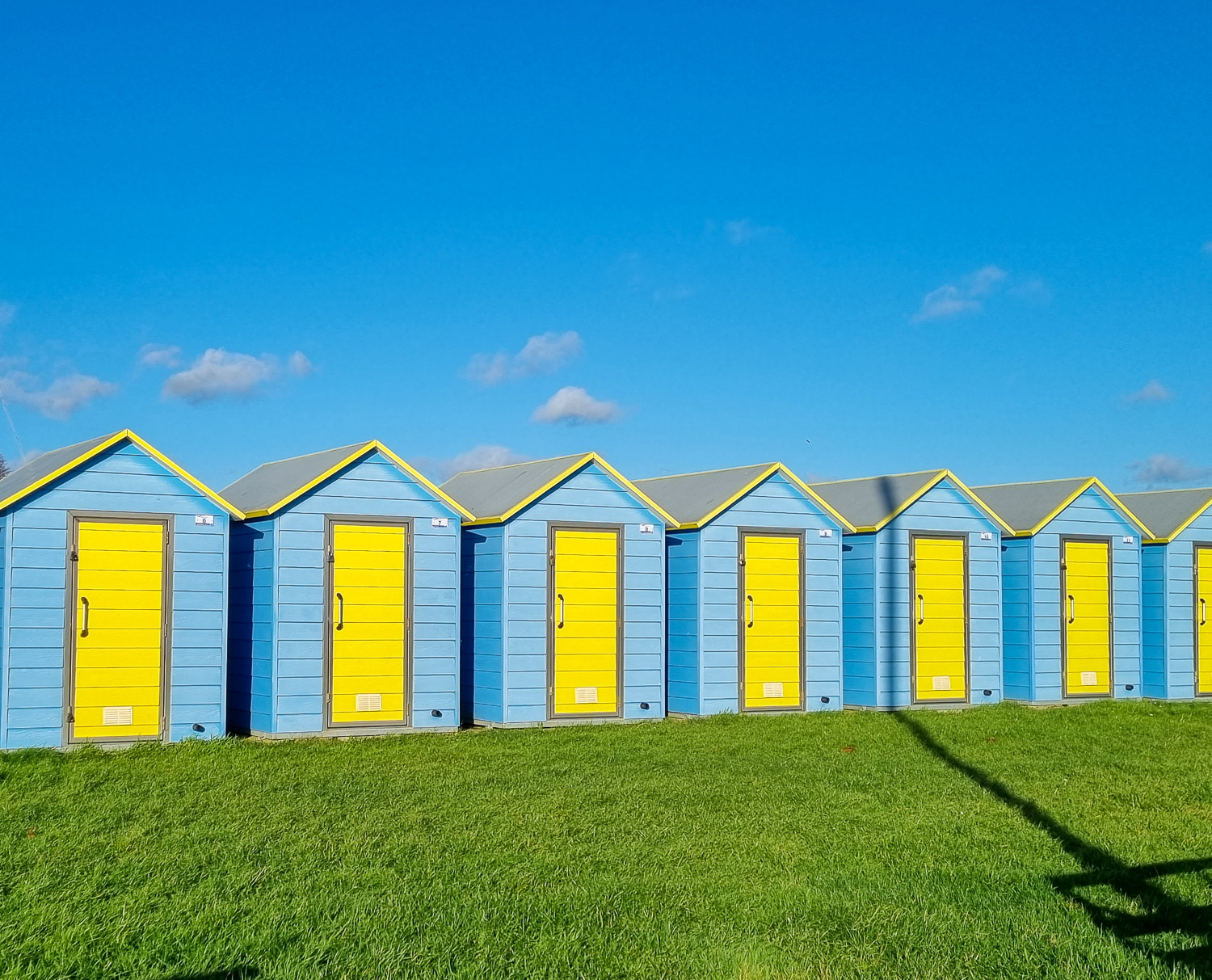 View of blue and yellow beach huts against a blue sky, by the beach at Felpham in west Sussex