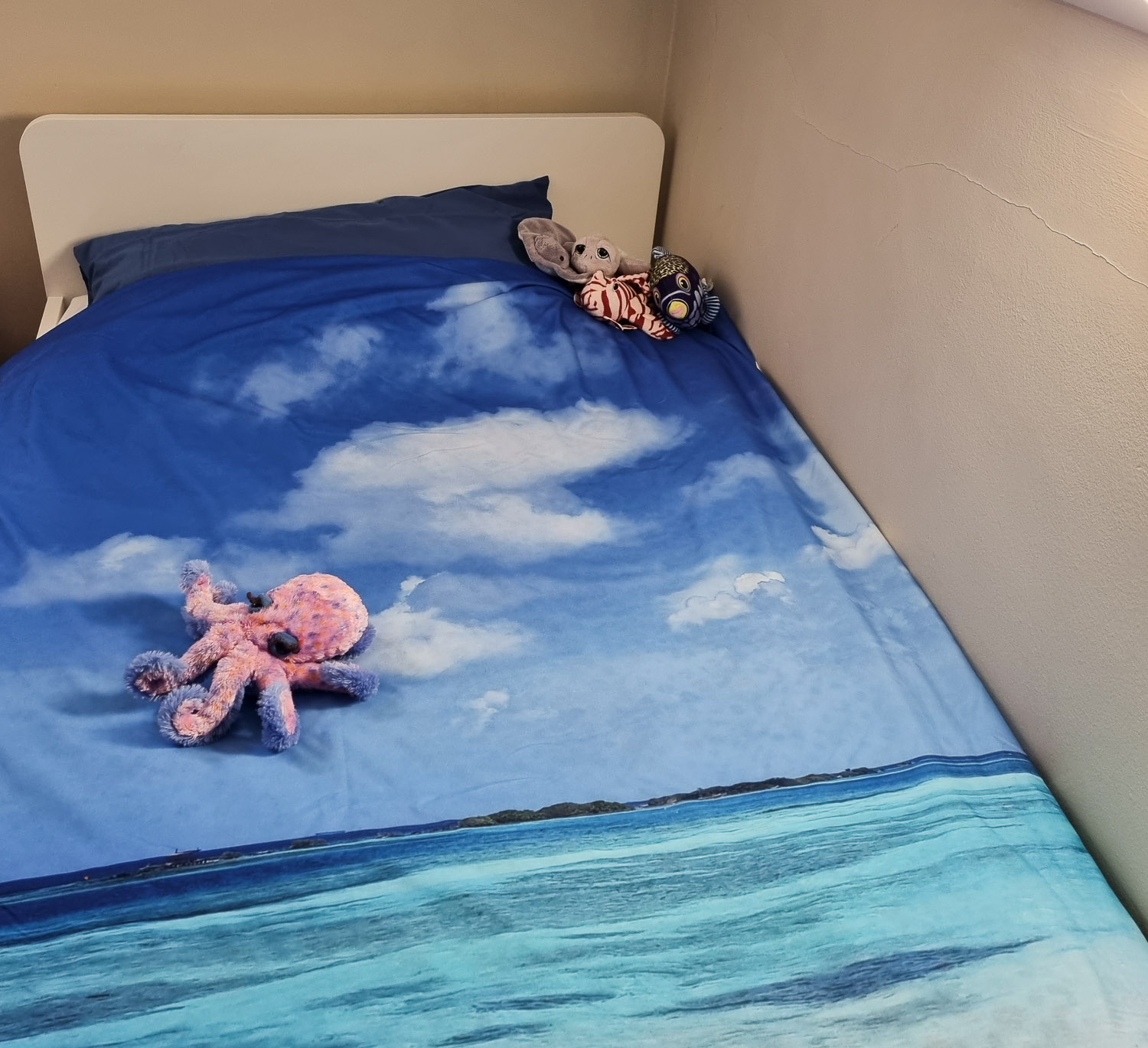 Stuffed animals, including fish and octopus on my daughter's bed showing duvet cover printed with a photo of the sea - a review of My Picture photo printing