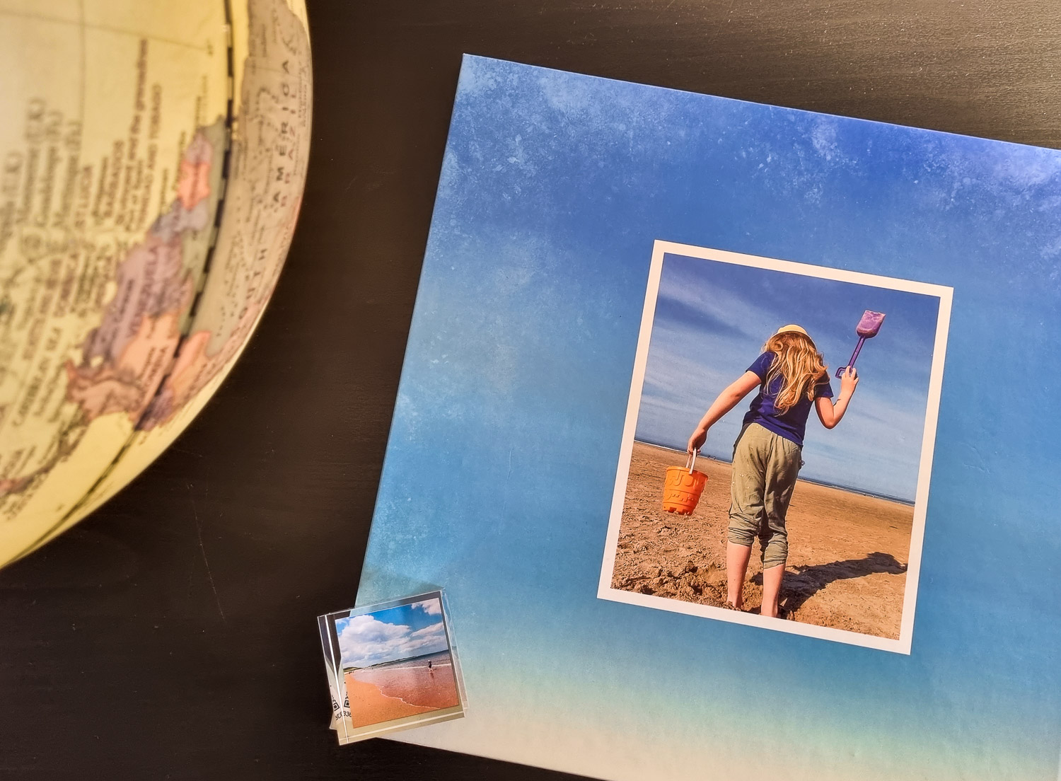 View of several products from the range of photo printed products including a MixBlox acrylic photo block lying on a photobook featuring a girl holding a spade on a beach, next to a globe - My Picture review