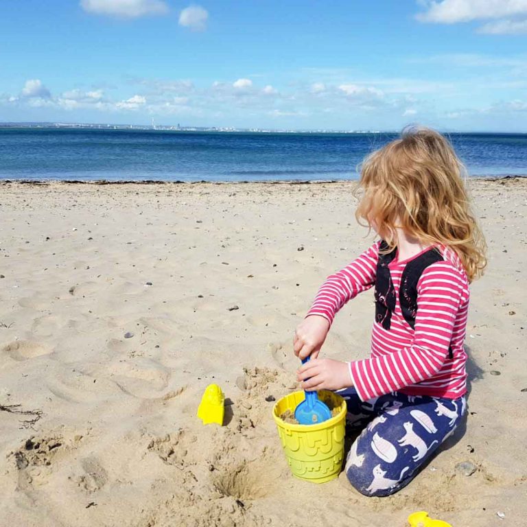 My daughter with bucket and spade on the beach at Appley near Ryde, looking back towards Portsmouth - my favourite beaches and more of the best things to do on the Isle of Wight with kids