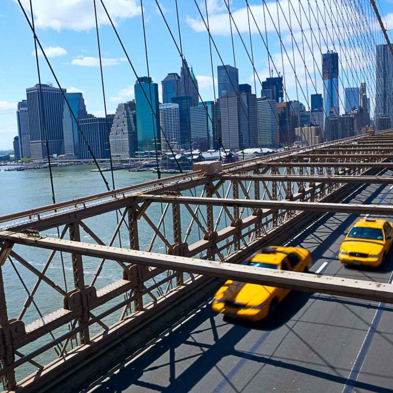 New York Manhattan skyline from the Brooklyn Bridge with yellow taxis driving out of the city - the best day trips from New York City with kids