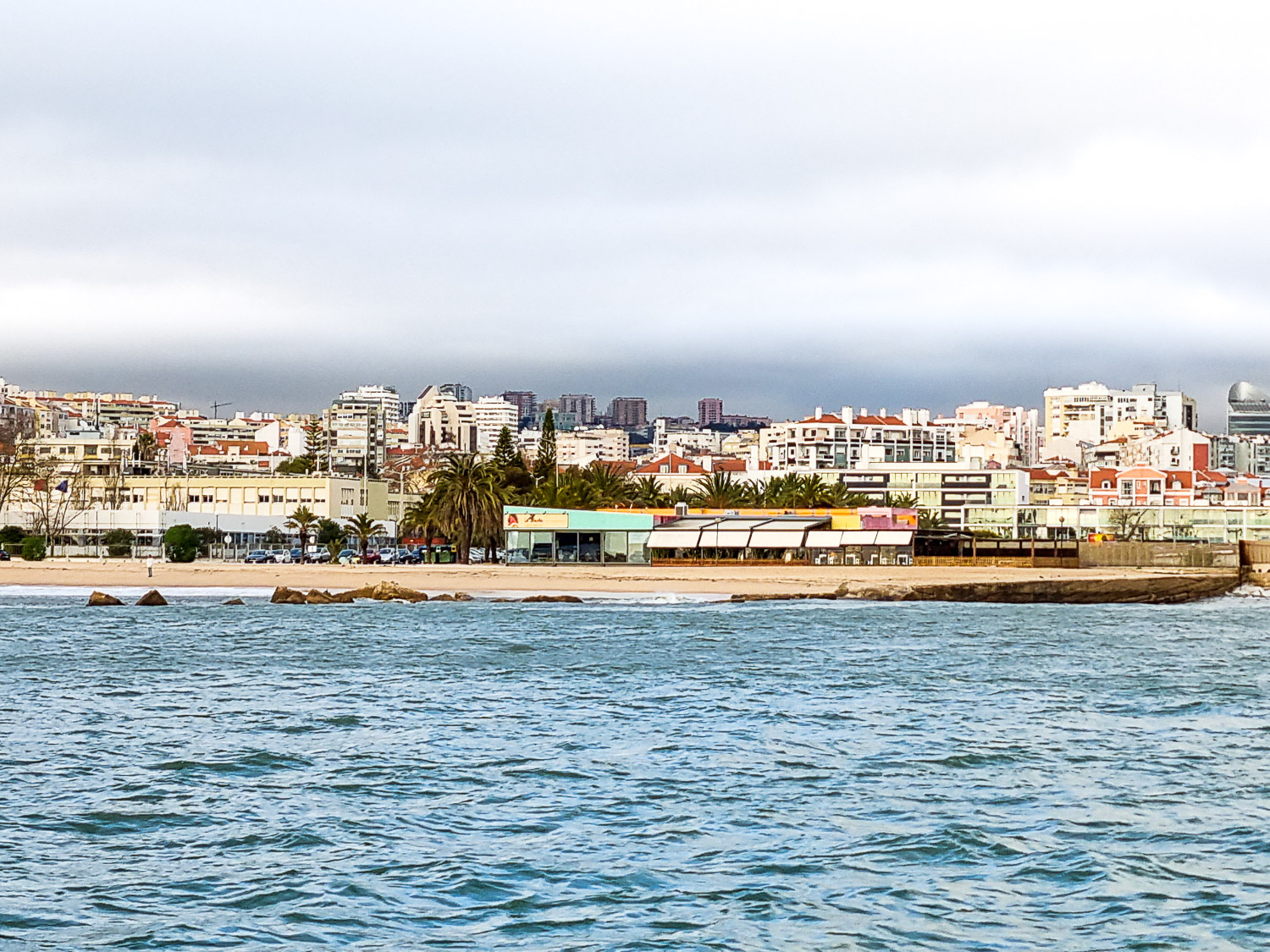 View of the riverside beach not far from Belem with brightly coloured buildings in the background - a quirky tour of Lisbon with kids for our Hippotrip review