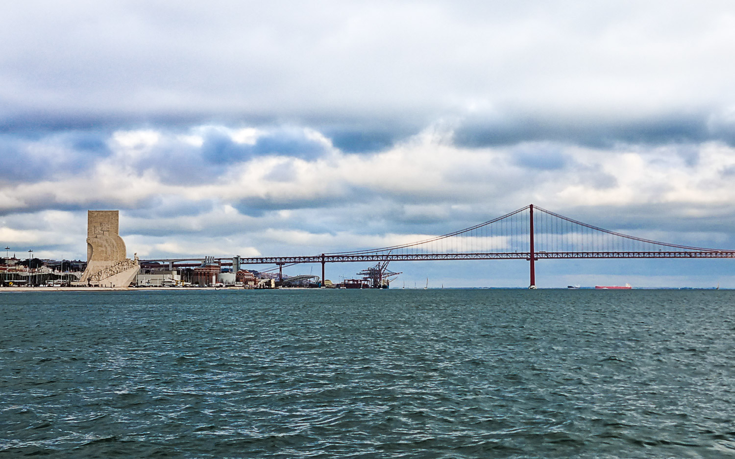 View of the bridge across the River Tagus in Lisbon seen from the water near Belem, with the Monument to the Discoveries on the bank - my Hippotrip review of a Lisbon boat tour with kids