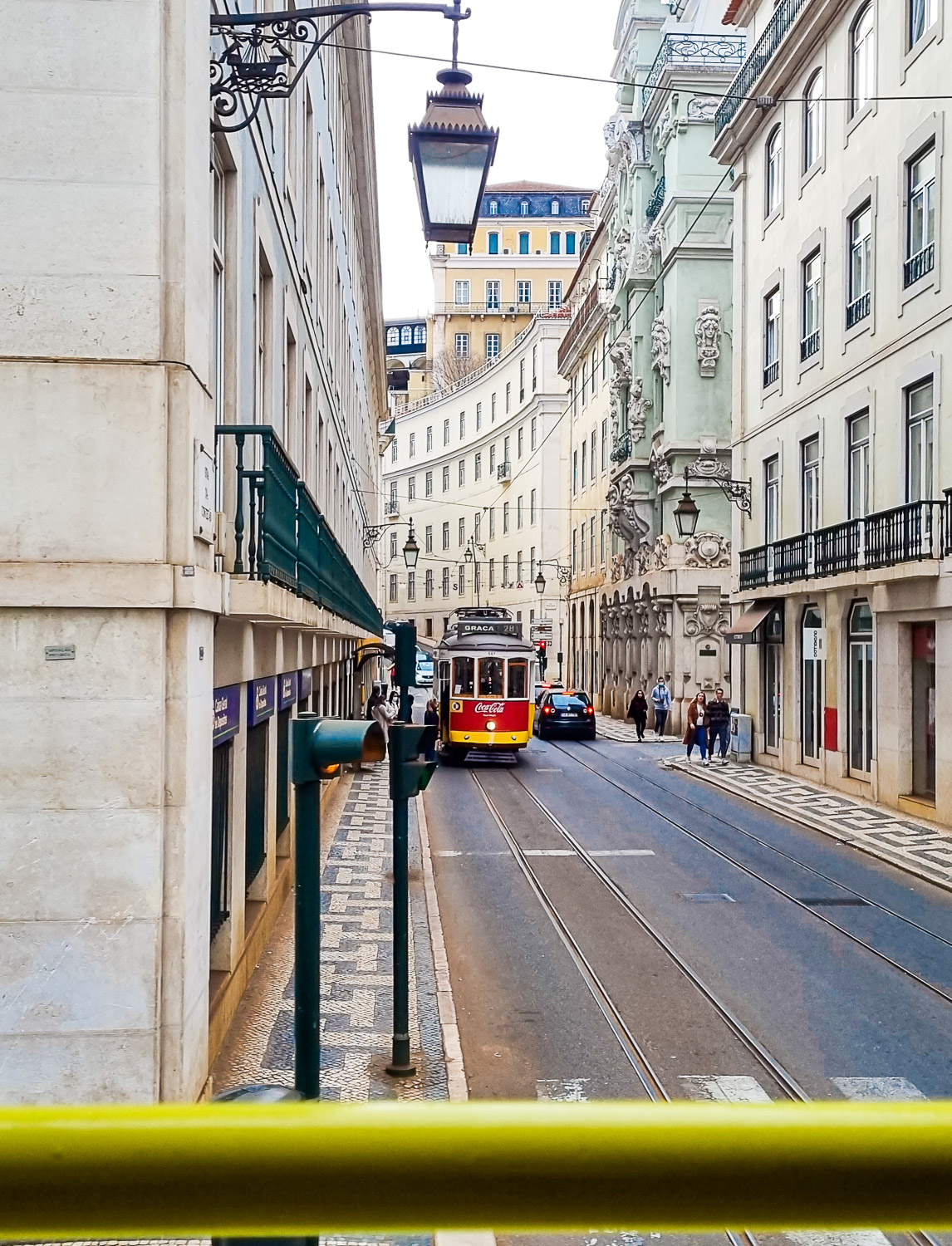 View over the yellow bar on the side of the Hippotrip amphibious vehicle of a tram in one of LIsbon's elegant side streets - my review of a Hippotrip tour of Lisbon with kids