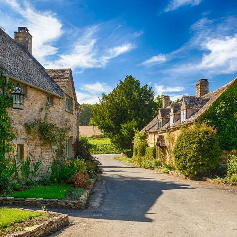 Street lined with honey coloured stone cottages under a blue sky in the Gloucestershire village of Icomb in the Cotswolds, one of the best days trips from London with kids