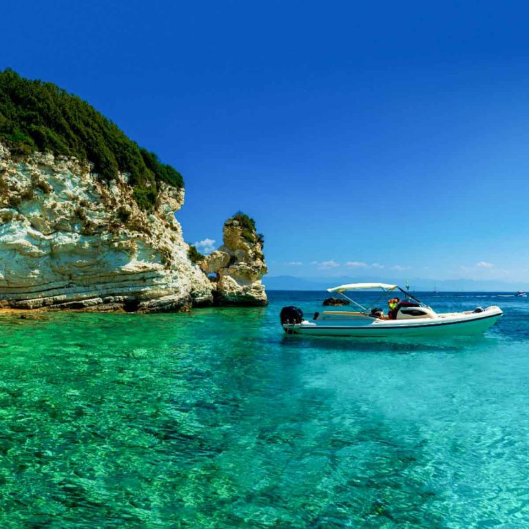 Boat on the clear turquoise green water of the Aegean near the island of Paxos, with yachts in the distance - my wishlist of which Greek islands with kids I'd like to visit