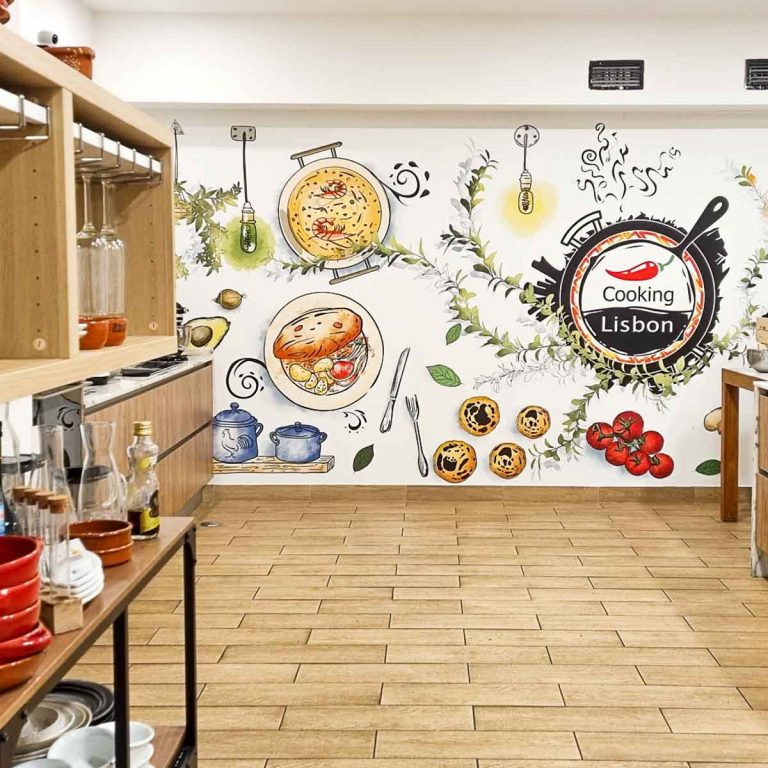 View of the Cooking Lisbon kitchen with bowls, oil and other ingredients on the shelves, bright mural on the wall, and worktops just seen - my review of our Lisbon cooking class with kids