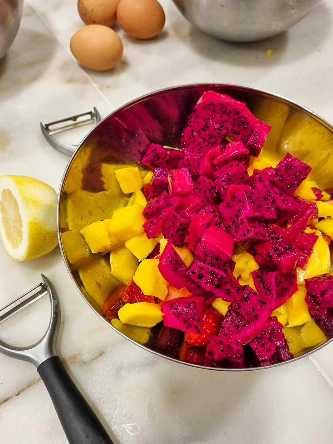 Silver bowl of bright orange mango and purple dragonfruit with lemon half, peelers and eggs just seen - some of the ingredients being prepared for our Lisbon cooking class with kids