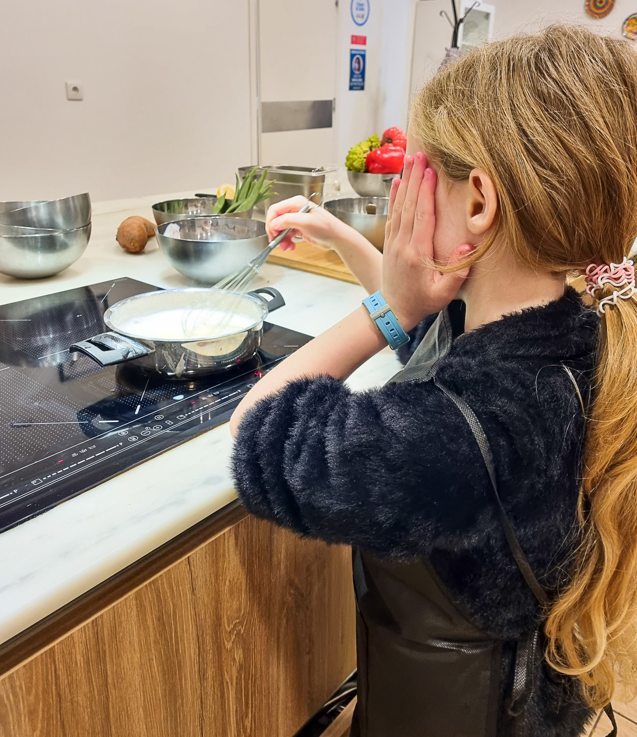 Young girl with blonde hair whisking a pan full of creamy liquid in the kitchen of Cooking Lisbon during our Lisbon cooking class with kids