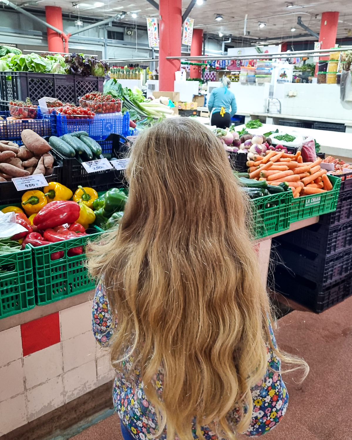 My daughter looks a some of the fresh vegetables on display at one of Lisbon's markets, including peppers, carrots, sweet potatoes and salad - my review of a Lisbon cooking workshop with kids
