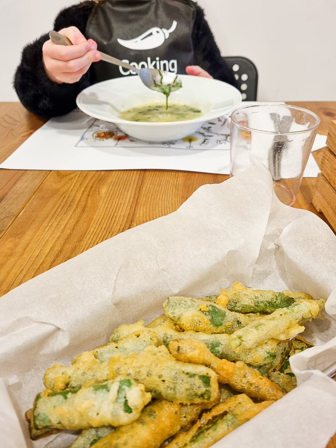 Basket of tempura green beans on a table with my daughter eating freshly made vegetable soup on the opposite side - enjoying our food after a Lisbon cooking class with kids